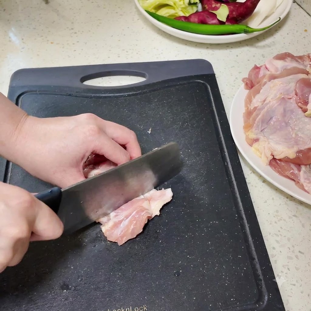 Ausgelöste Hähnchenunterkeulen werden auf einem schwarzen Schneidebrett in kleinere Stücke gehackt.