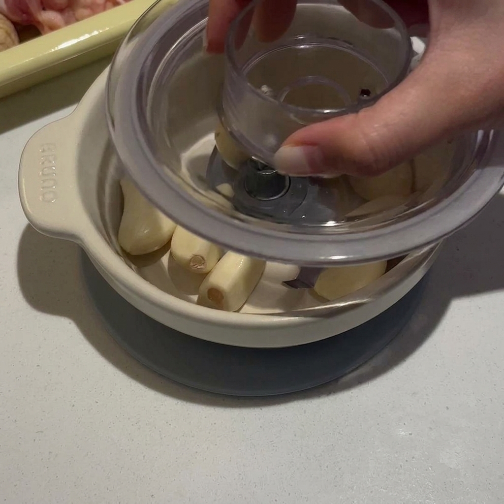 Eine Person drückt auf den Deckel eines kleinen manuellen Zerkleinerers voller geschälter Knoblauchzehen.