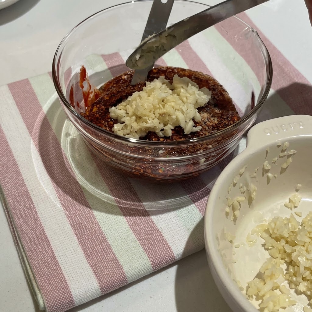 Koreanische Chilipaste und verschiedene Gewürze werden in einer Glasschüssel zu einer dicken roten Sauce verrührt.
