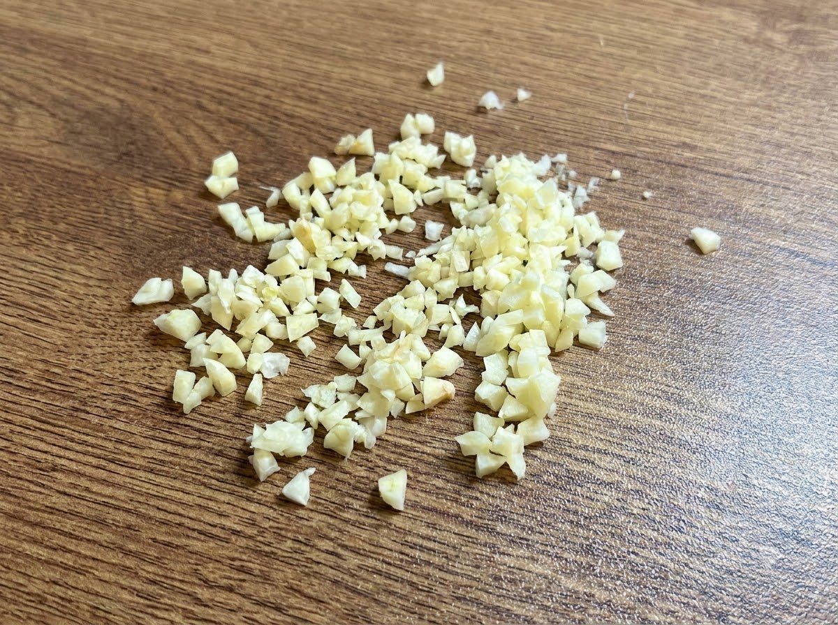 Ein kleiner Haufen fein gehackter frischer Knoblauch auf einem Holzschneidebrett.