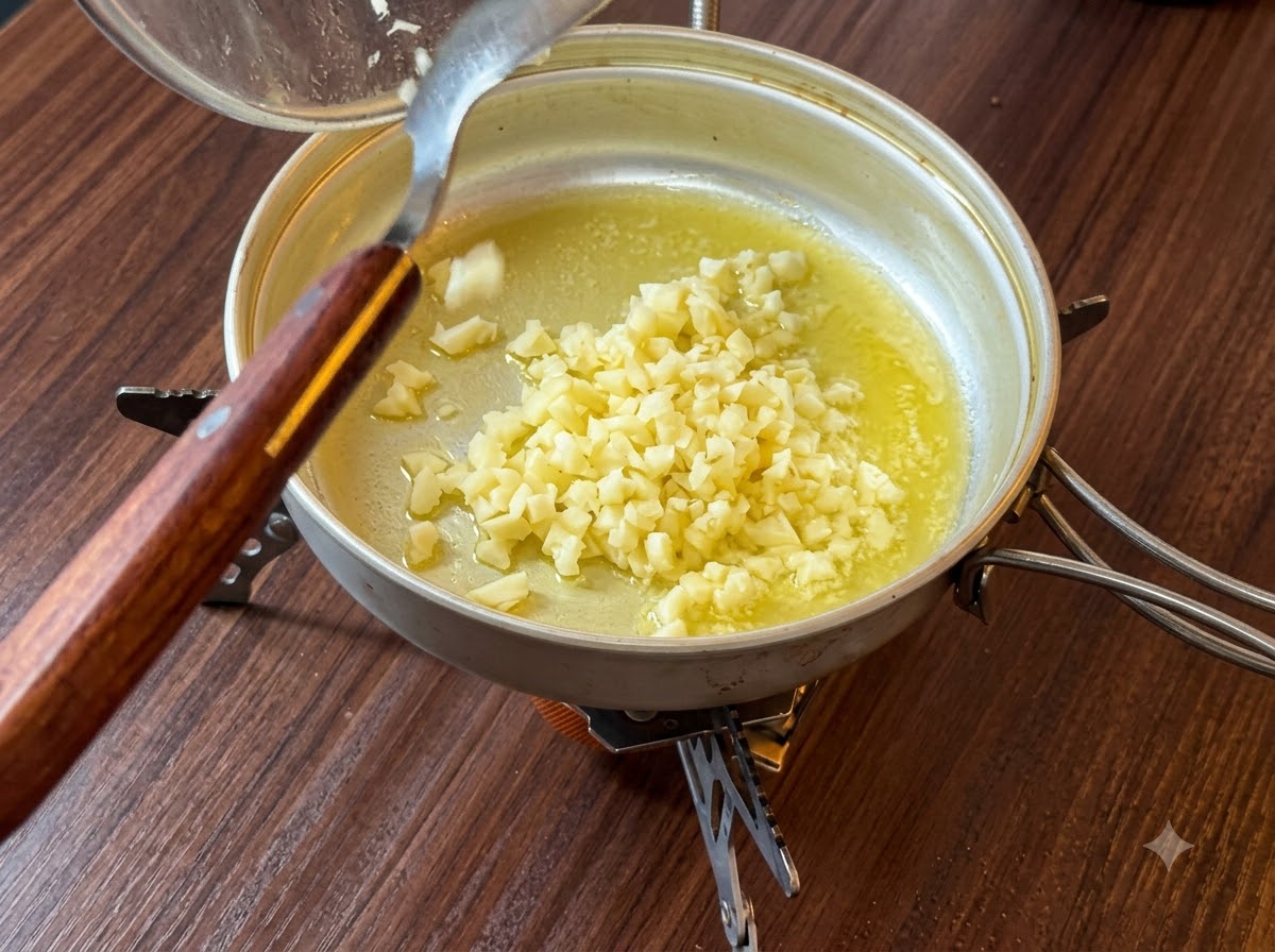 Fein gehackter Knoblauch wird aus einem Behälter in die geschmolzene Butter in einer Pfanne gegeben.