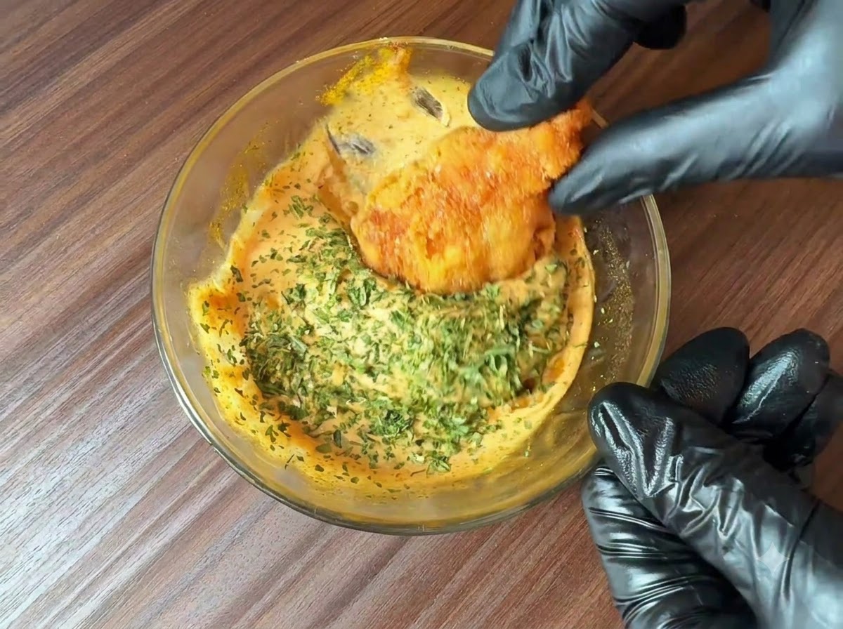 Frisch gehackte Petersilie wird über eine Schüssel mit zubereiteter Burgersauce gestreut, während ein frittiertes Stück darin eingetaucht wird.