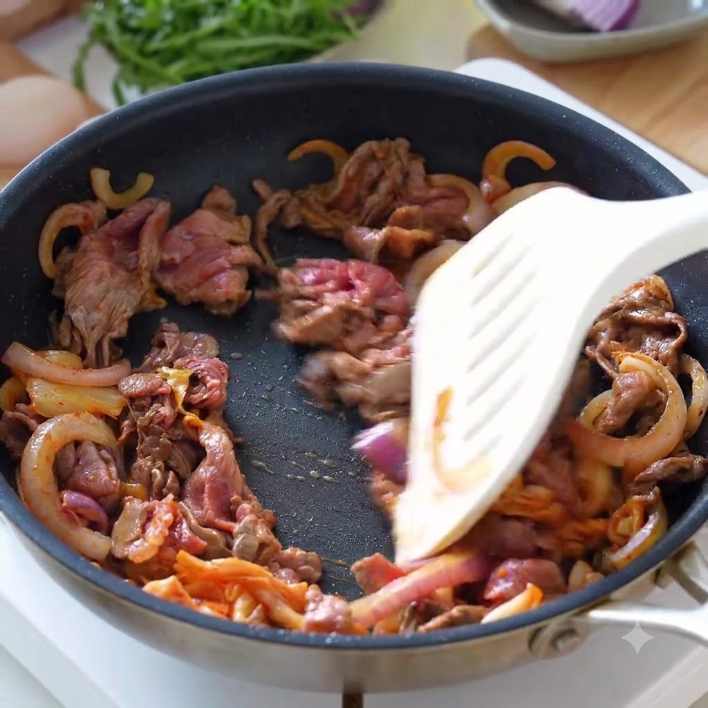 Geschnittenes Rindfleisch, Zwiebeln und Kimchi werden mit einem Spatel in einer Pfanne vermengt.