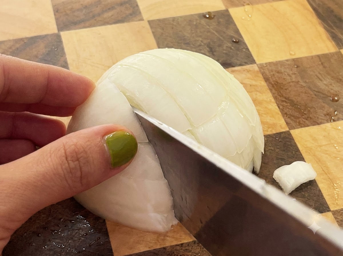 Ein Messer schneidet durch eine halbierte weiße Zwiebel auf einem karierten Holzschneidebrett.