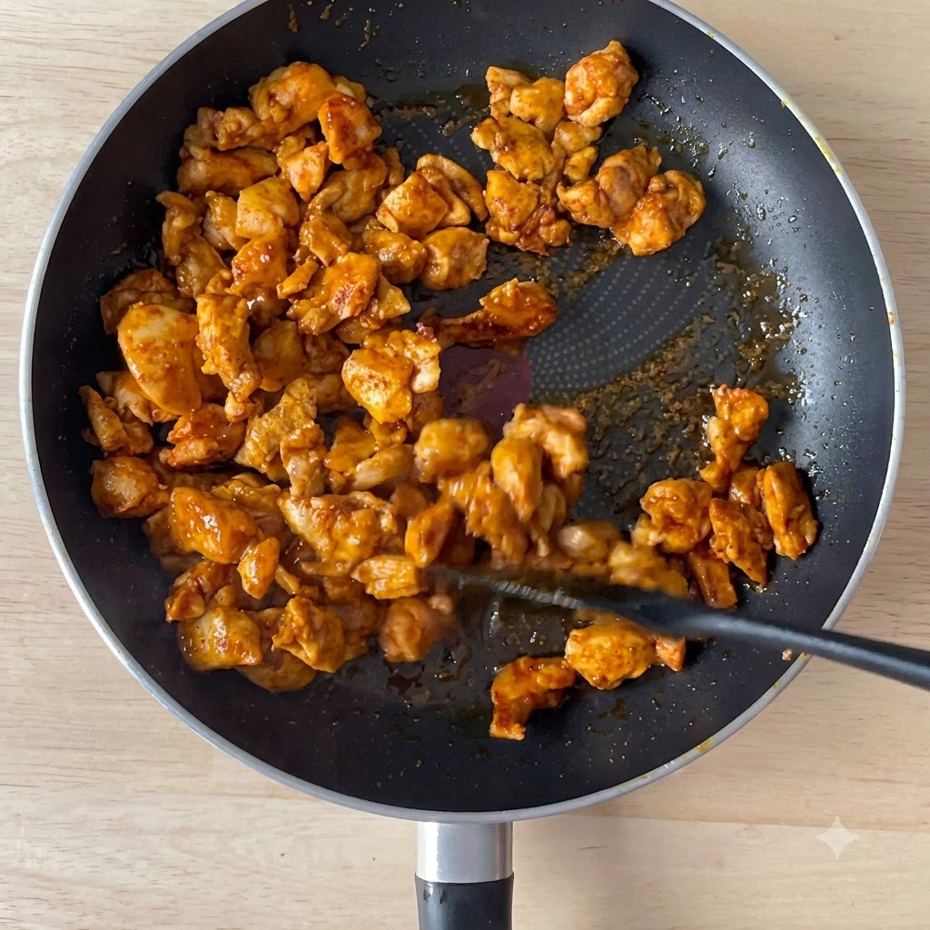 Sojasoße wird in eine Pfanne mit angebratenen Hähnchenstückchen gegossen.