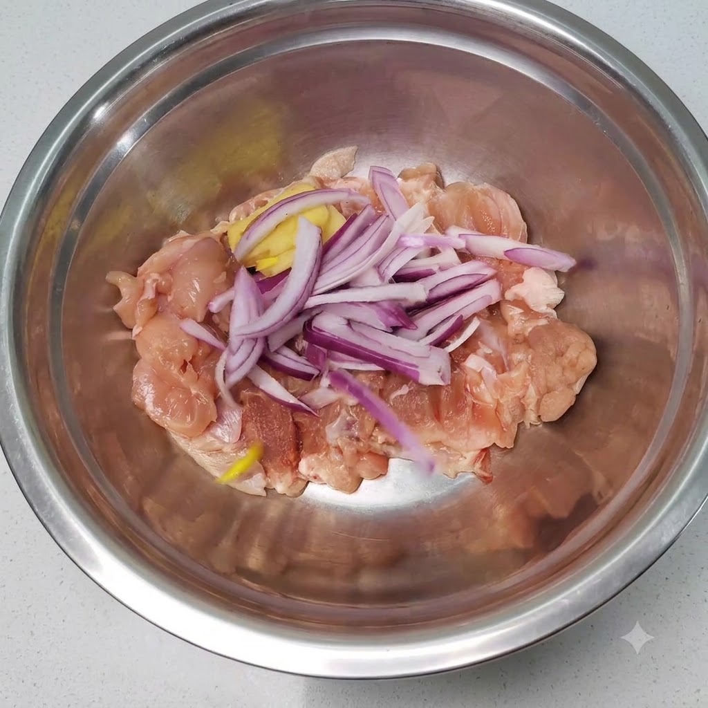 Rohe Hähnchenstücke gemischt mit in Scheiben geschnittenen roten Zwiebeln und Ingwer in einer Edelstahlschüssel.