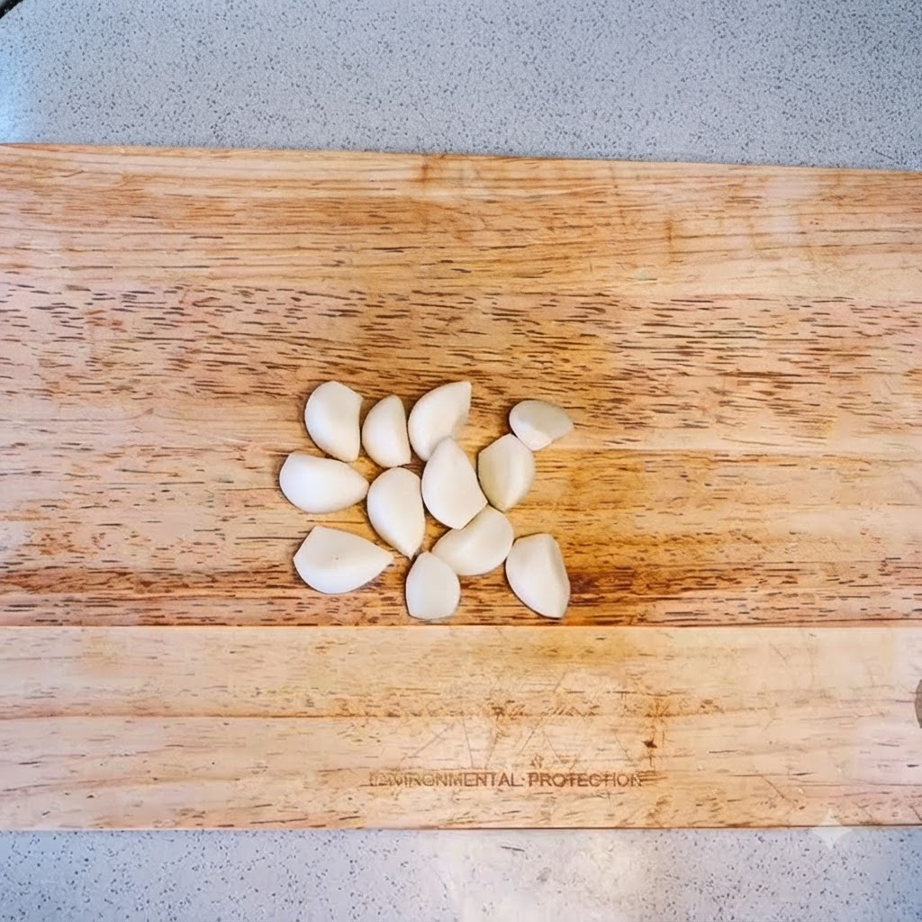 Knoblauchzehen auf einem Holzschneidebrett angeordnet, bereit zum Hacken.
