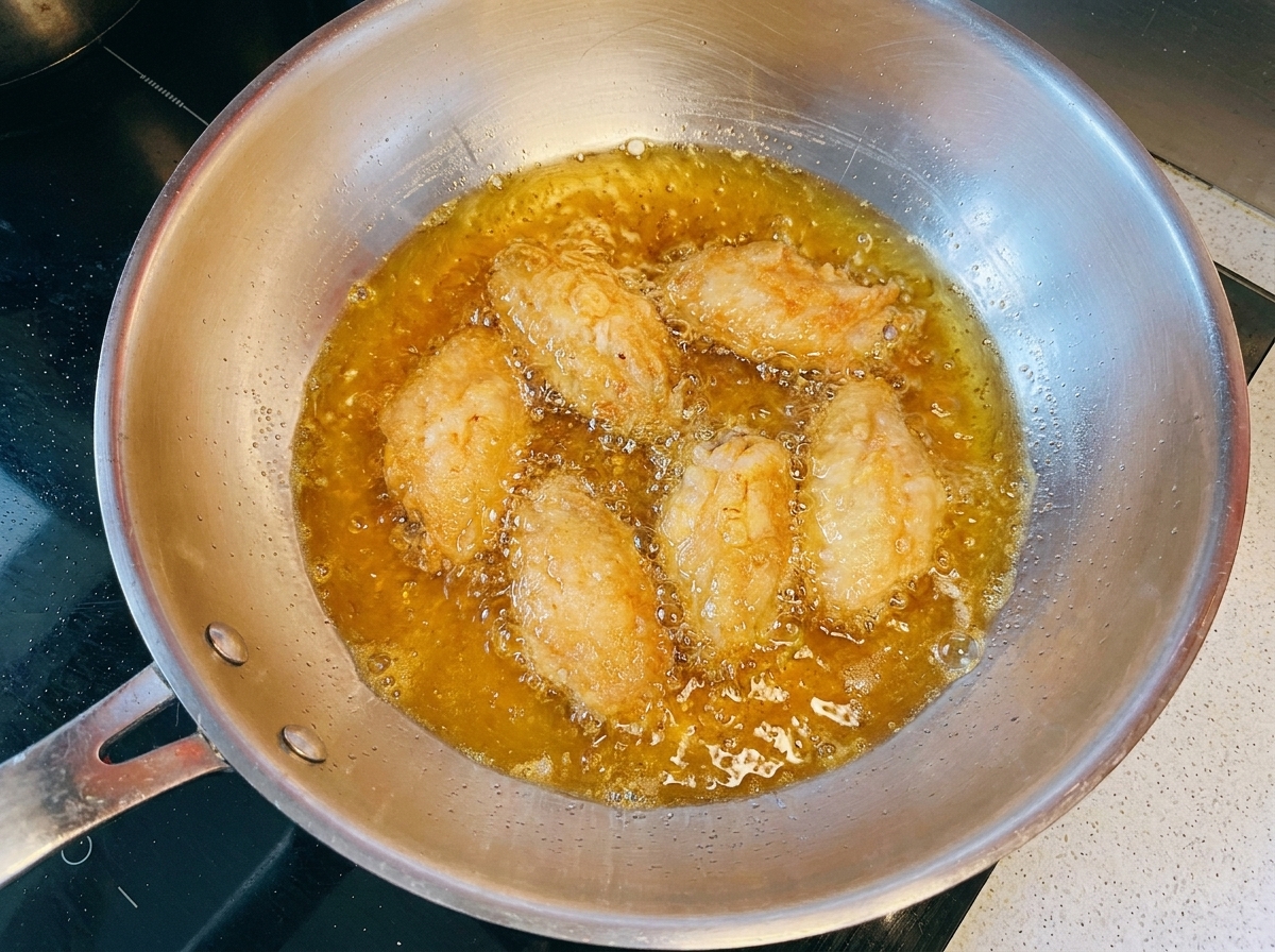 Goldbraune Hähnchenflügel frittieren in heißem Öl in einer Metallpfanne.