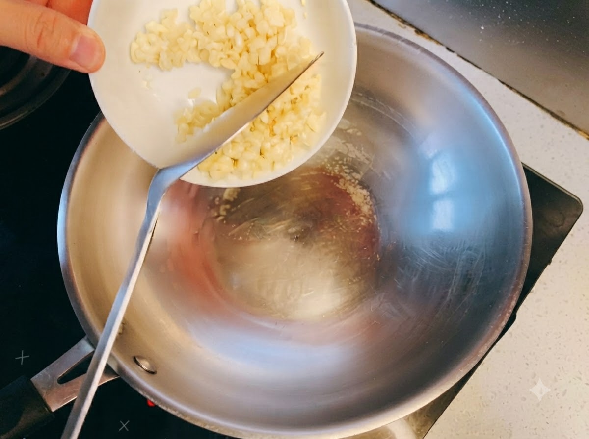 Gehackter Knoblauch trifft in einem Edelstahl-Wok auf heißes Öl und beginnt zu brutzeln.
