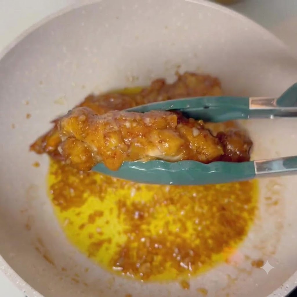 Eine Zange hält eine glasierte Hähnchenkeule über eine Pfanne mit blubbernder Knoblauch-Butter-Sauce.